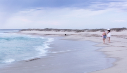 Abstract photo of people walking dog along a beach - Australian Stock Image