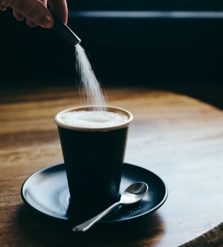 Action of pouring a sachet of sugar into a cafe latte at a restaurant - Australian Stock Image