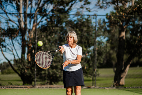 Active elderly female tennis player hitting a ball with a racquet - Australian Stock Image