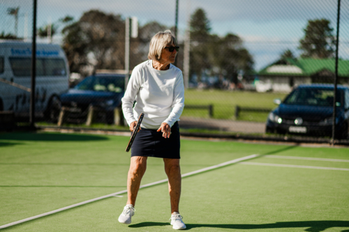 Active older woman participating in a tennis game on a vibrant outdoor court - Australian Stock Image