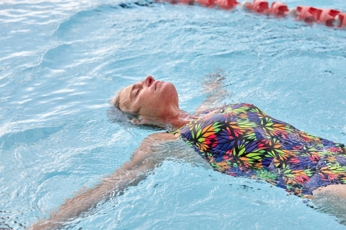 Active senior lady floating in swimming pool - Australian Stock Image