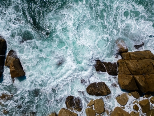 Active waves crashing against the rocky shore creating a foamy surface on the water - Australian Stock Image