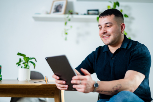 Adult man engages with a tablet in a stylish living space, smiling as he explores content - Australian Stock Image