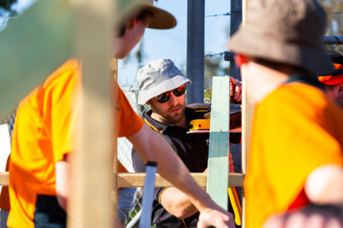 Adult tradesman teaching teen apprentices during hands on building skills class - Australian Stock Image