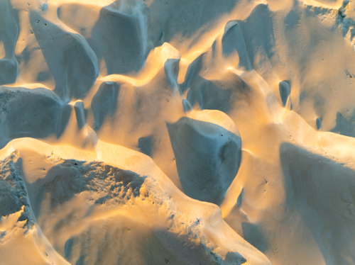 Aerial close-up of sculpted sand dunes with golden light and shadow creating abstract patterns - Australian Stock Image