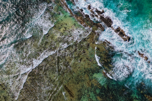 Aerial downward view of ocean waves crashing over the rugged rocky coastline at Brooms Head - Australian Stock Image