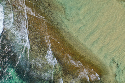 Aerial downward view of ocean waves crashing over the rugged rocky coastline at Brooms Head - Australian Stock Image