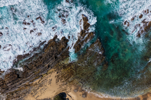 Aerial downward view of ocean waves crashing over the rugged rocky coastline at Brooms Head - Australian Stock Image