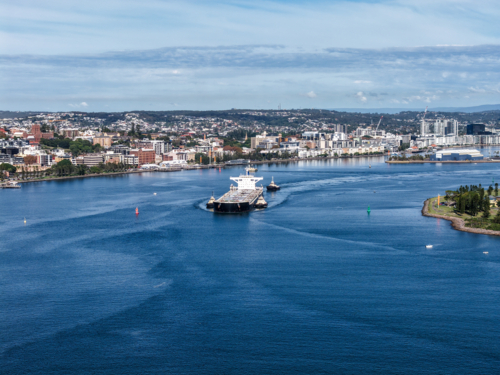 Aerial drone view of a large cargo ship being escorted by tug boats through Newcastle Harbour. - Australian Stock Image