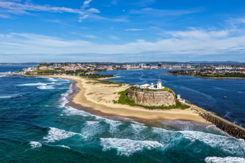 Aerial drone view of Nobbys Lighthouse and sandy Nobbys Beach with Newcastle city skyline. - Australian Stock Image