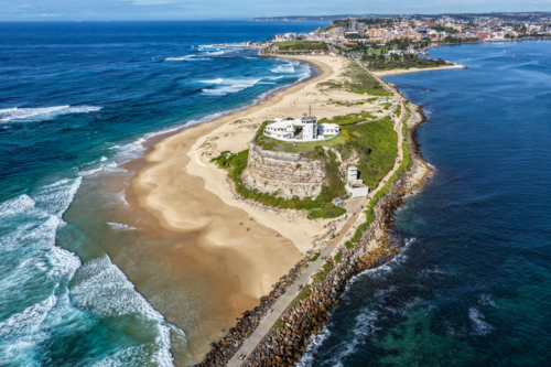 Aerial drone view of Nobbys Lighthouse and sandy Nobbys Beach with Newcastle harbour. - Australian Stock Image