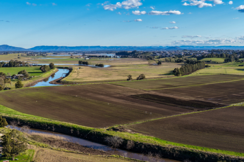 Aerial drone view of rural farmland in Maitland, New South Wales, Australia beneath cloudy blue sky - Australian Stock Image