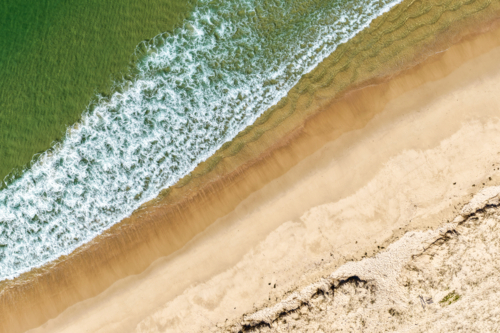 Aerial image capturing waves rolling onto the sandy shoreline of Nine Mile Beach in Tuncurry - Australian Stock Image