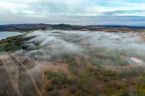 Aerial image of the Glenbawn Dam wall with morning fog drifting through the surrounding valley - Australian Stock Image