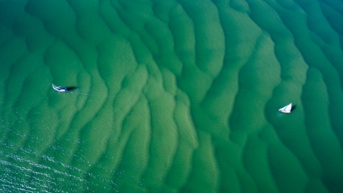 Aerial image of two small sailboats sailing over rippled sandbars.