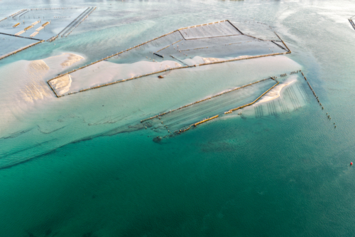 Aerial image showcasing the bright turquoise waters of Wallis Lake at low tide with patterns in sand - Australian Stock Image