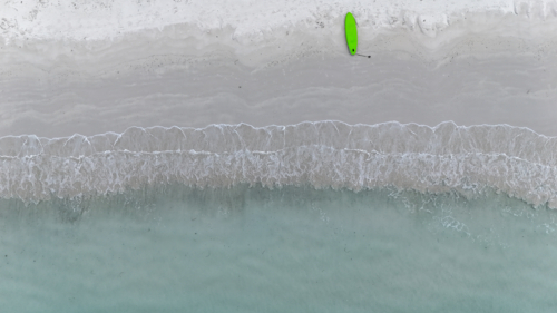 Aerial of a paddle board laying on the sand at the shoreline - Australian Stock Image