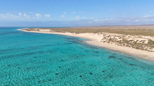Aerial of a remote beach with turquoise water surrounded by sand dunes - Australian Stock Image