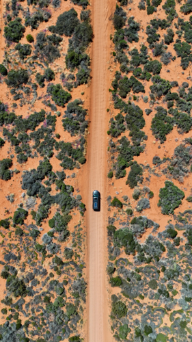 Aerial of car driving along straight red dirt road - Australian Stock Image