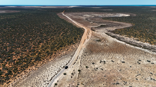 Aerial of car driving on a road through a clay pan - Australian Stock Image