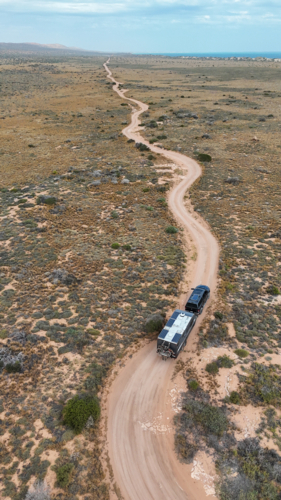 Aerial of caravan driving along bending dirt road - Australian Stock Image