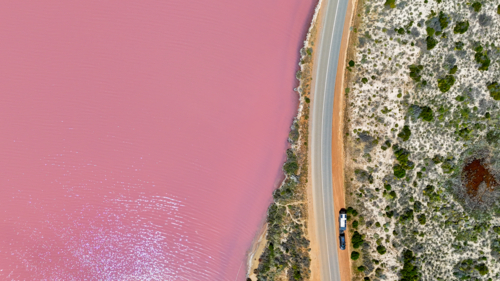 Aerial of caravan on road next to pink lake - Australian Stock Image
