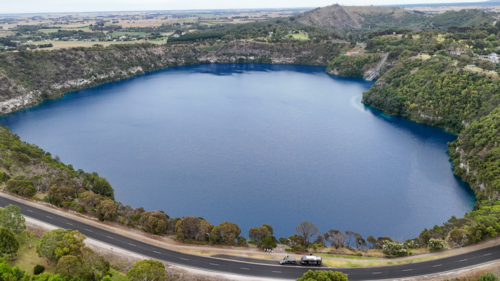 Aerial of caravan parked up next to big blue lake in a town - Australian Stock Image