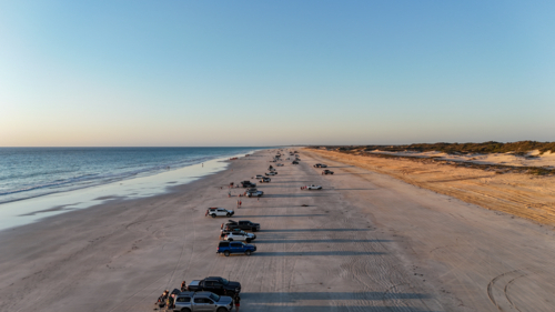Aerial of cars parked up along beach at sundown - Australian Stock Image