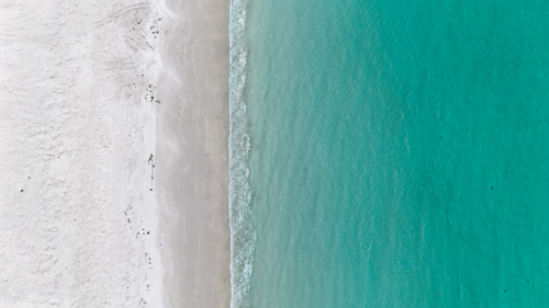 Aerial of clear blue water meeting white sand - Australian Stock Image
