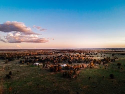 Aerial of flat land, trees, 2 small sheds with blue sky and clouds - Australian Stock Image