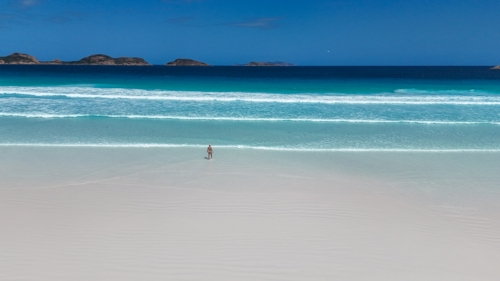 Aerial of girl walking into water at beach with white sand and crystal blue water - Australian Stock Image