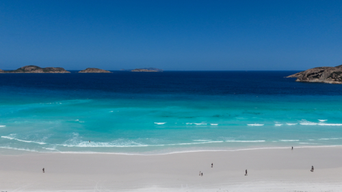 Aerial of people walking along beach either white sand and crystal blue water - Australian Stock Image