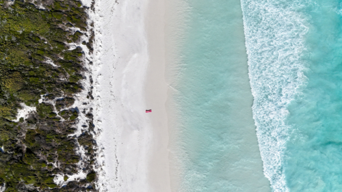 Aerial of person laying on pink towel on beach with crystal blue water - Australian Stock Image