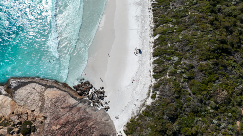 Aerial of remote beach with big rock, white sand, clear blue water and bush - Australian Stock Image