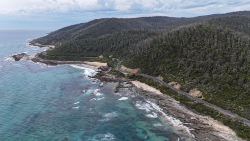 Aerial of road at bottom of mountains next to ocean - Australian Stock Image