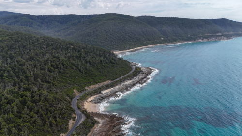 Aerial of road bending along mountains by the ocean - Australian Stock Image