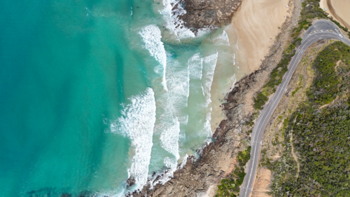 Aerial of road bending around beach with waves - Australian Stock Image