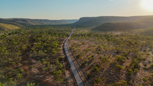 Aerial of road through forest landscape at golden hour - Australian Stock Image
