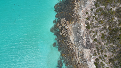 Aerial of rocky edge meeting bright aqua water - Australian Stock Image