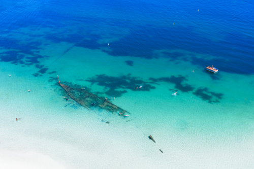 Aerial of shipwreck can be seen in the crystal clear ocean near local beach - Australian Stock Image