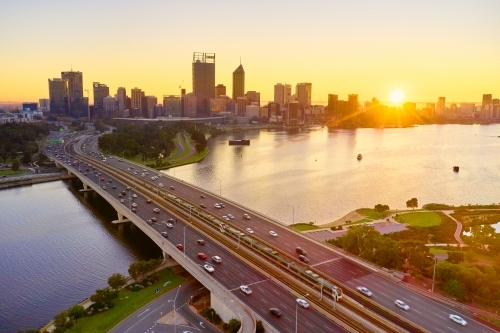 Aerial of the sunrise over the Perth skyline with morning traffic on the Narrows Bridge and river.