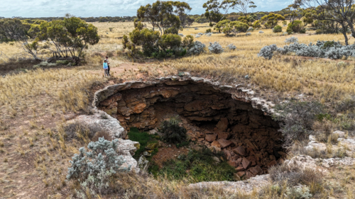 Aerial of two kids looking into a remote sinkhole - Australian Stock Image