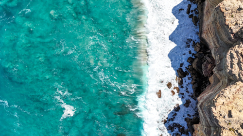 Aerial of waves crashing at the bottom of coastal cliffs - Australian Stock Image