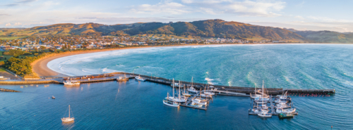 Aerial panorama of boats in a coastal harbour in front of a seaside town and hills - Australian Stock Image
