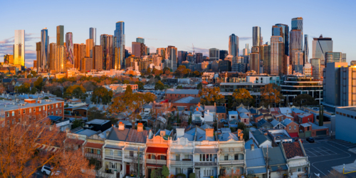 Aerial panorama of terrace houses in a suburban street in front of a city skyline in golden light - Australian Stock Image