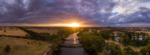 Aerial panorama view of colourful dramatic sunset over farmland alongside an inland river and bridge - Australian Stock Image