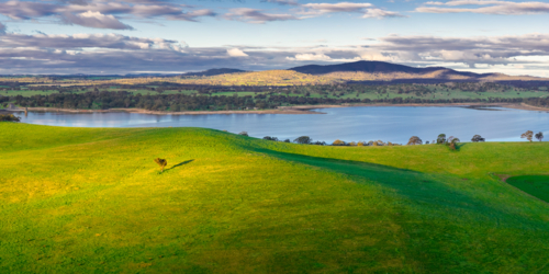 Aerial panorama view of sunshine on lush green hills around an inland lake and distant hills - Australian Stock Image
