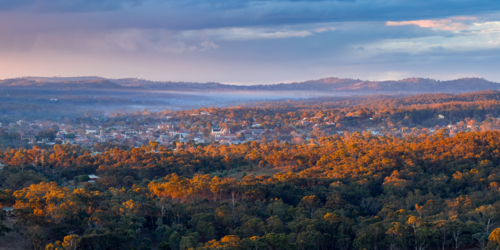 Aerial panorama view of twilight colours and golden light over a rural town nestled in forest valley - Australian Stock Image