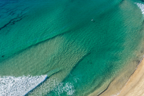 Aerial scene capturing a lone paddleboard rider in the clear turquoise waters at One Mile Beach. - Australian Stock Image