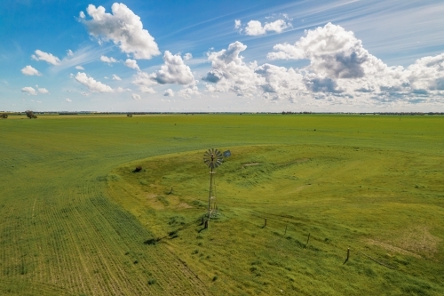 aerial shot of a big open field with a windmill under cloudy blue skies